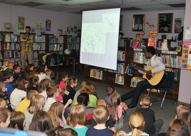 Alpha Rwirangira, left, plays guitar and sings at Taylor County Elementary School. Dr. DeWayne Frazier, right, spoke of his adventures in Rwanda where Rwirangira is from. (Campbellsville University Photo by Elaine Tan)