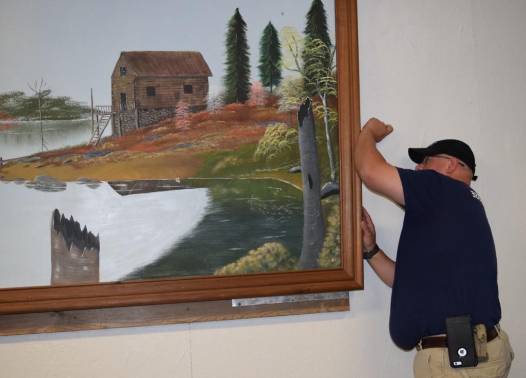 Damon Graham, son of Myna Graham and the late Jerry Graham, takes down the painting his father painted and that hung in Campbellsville University's Physical Plant for several years. (Campbellsville University Photo by Jesse Harp)