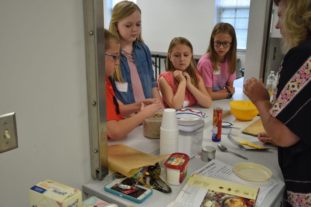 Pam Tennant, left, leads the Kids College Cooking up a Storm class on Campbellsville University’s campus. Tennant shows, from left, Chloe Thompson of Campbellsville, Ky., Emily VanHoosier of Lebanon, Ky., Gabriella VanHoosier of Lebanon, Ky., and Jaxon McCubbin of Campbellsville, Ky. how to measure their ingredients for their recipe of the day. (Campbellsville University Photo by Ariel Emberton)